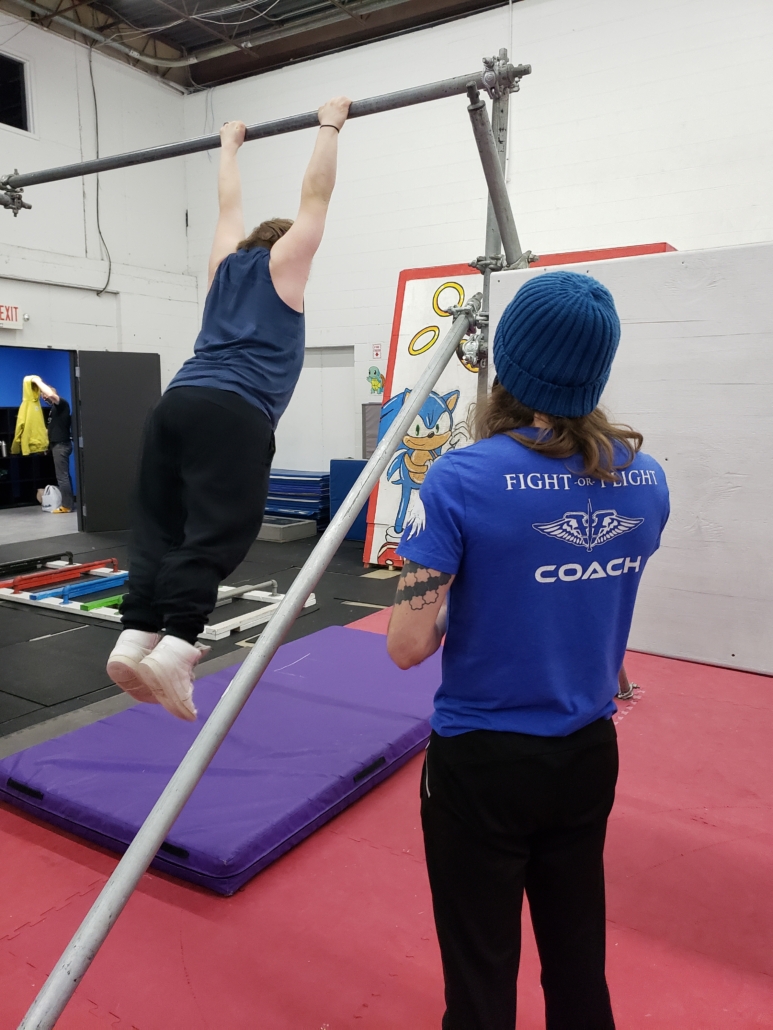 Parkour coach Tom watching student swing on bar